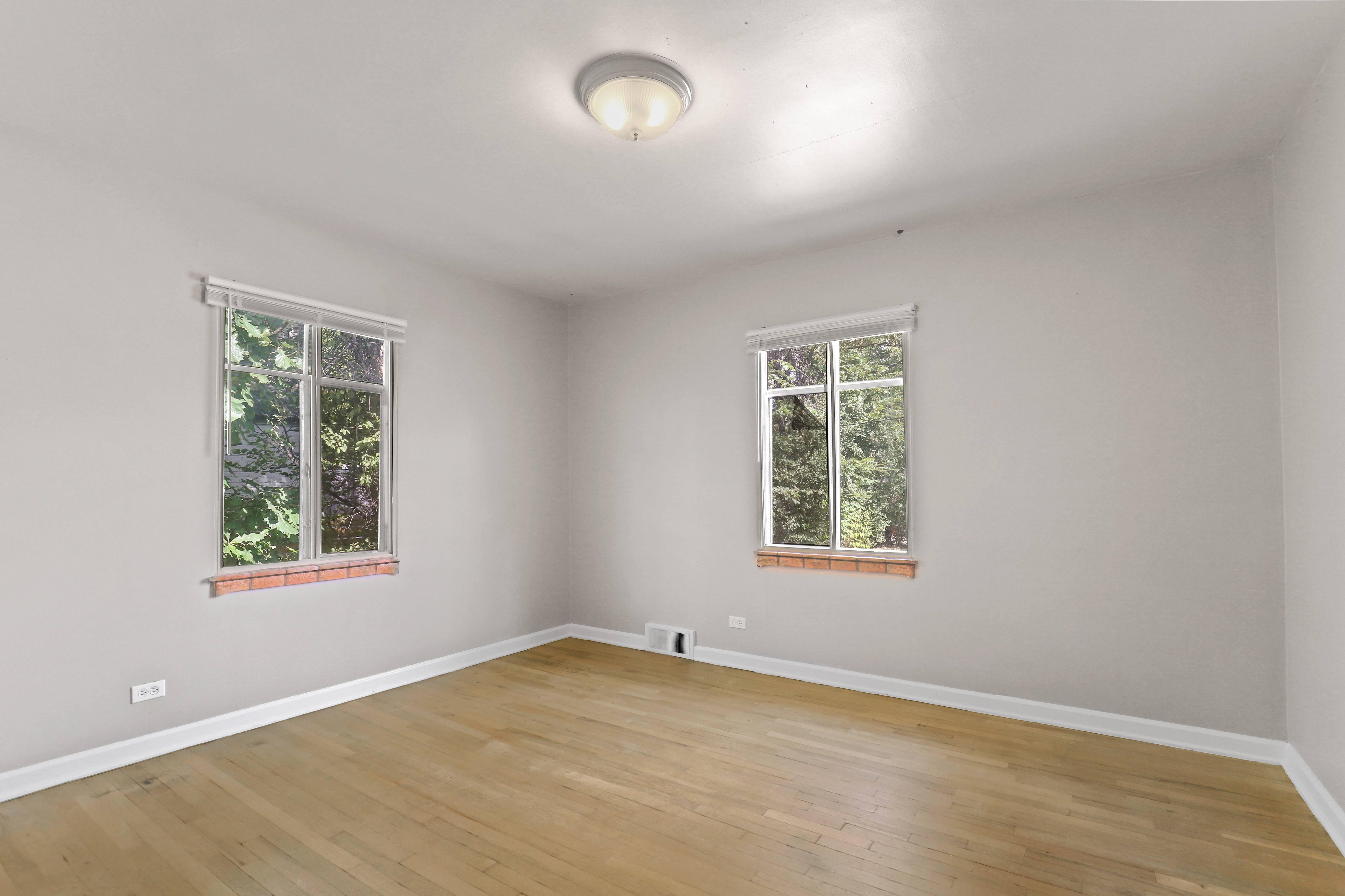 an empty room with wooden floors and two windows